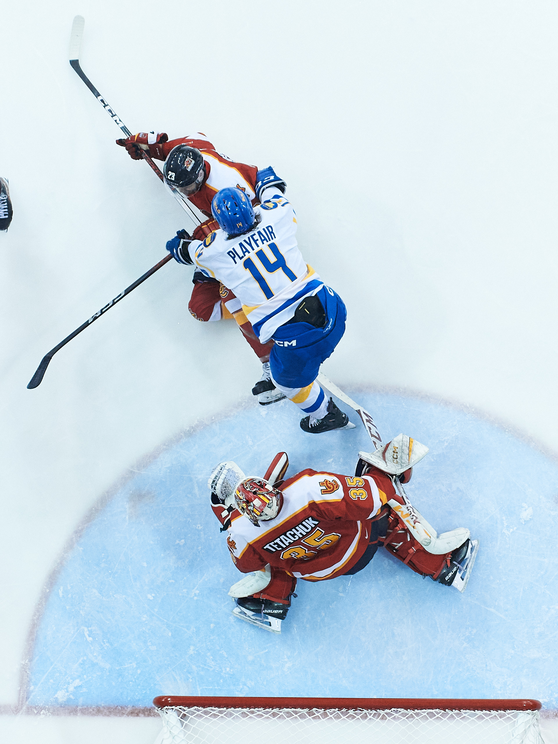 An overhead shot of a TMU hockey player cross-checking a Calagary player in front of the Dinos net