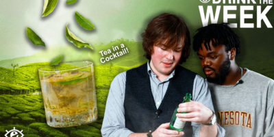 to the left a beige drink with green leaves falling into it to the right text that reads "tea in a cocktail!" to the right are Jake and divine both looking intently at a green glass bottle