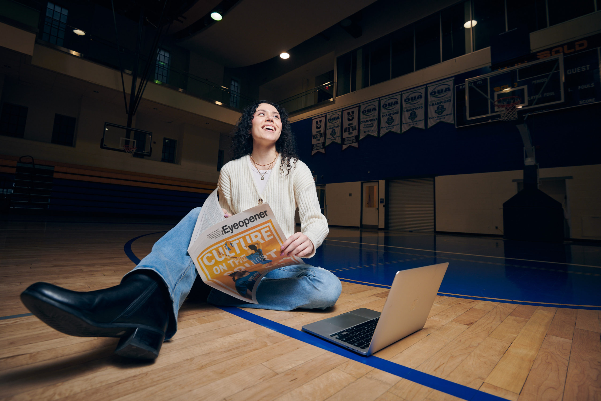 A woman sits on a basketball court holding a newspaper