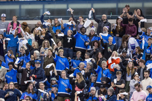 Fans in blue PWHL Toronto jerseys swing rally towels in the air in the stands at a game