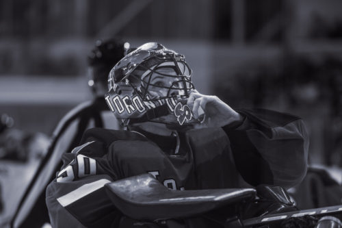 A black and white photo of Toronto goaltender Kristen Campbell adjusting her helmet and looking upward