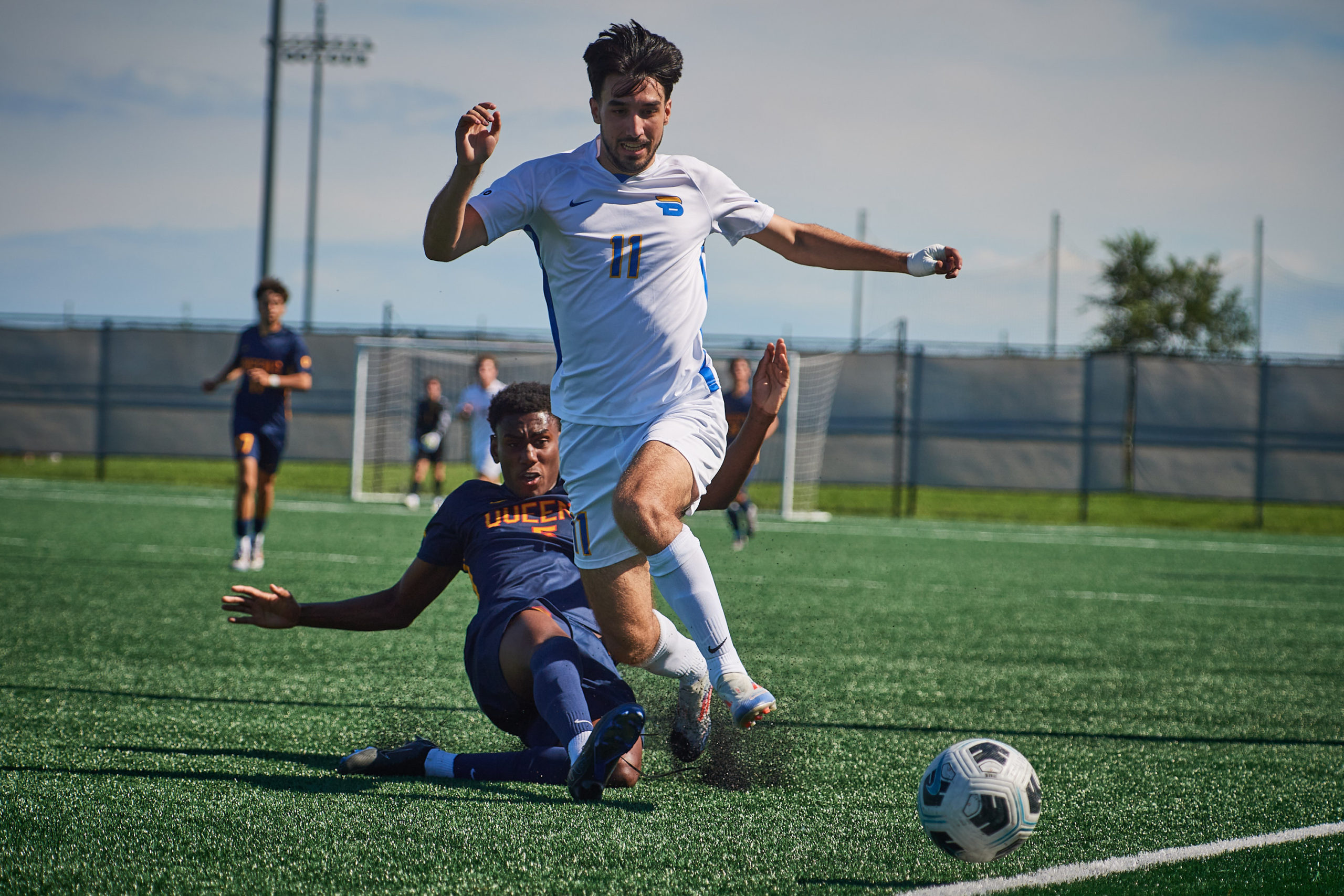 A Queen's men's soccer player slide tackles he ball away from the feet of TMU Bold player Justin Santos