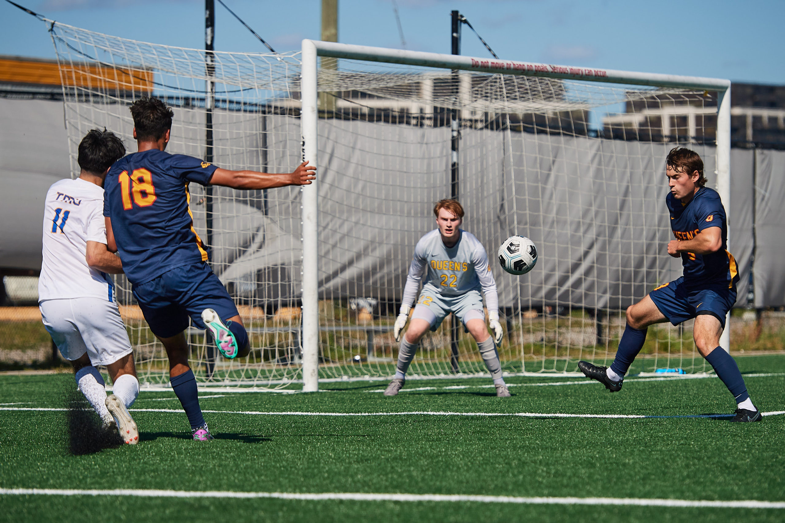 A TMU Bold player shoots a soccer ball towards a Queen's Gaels goalie. Other Queen's players are around