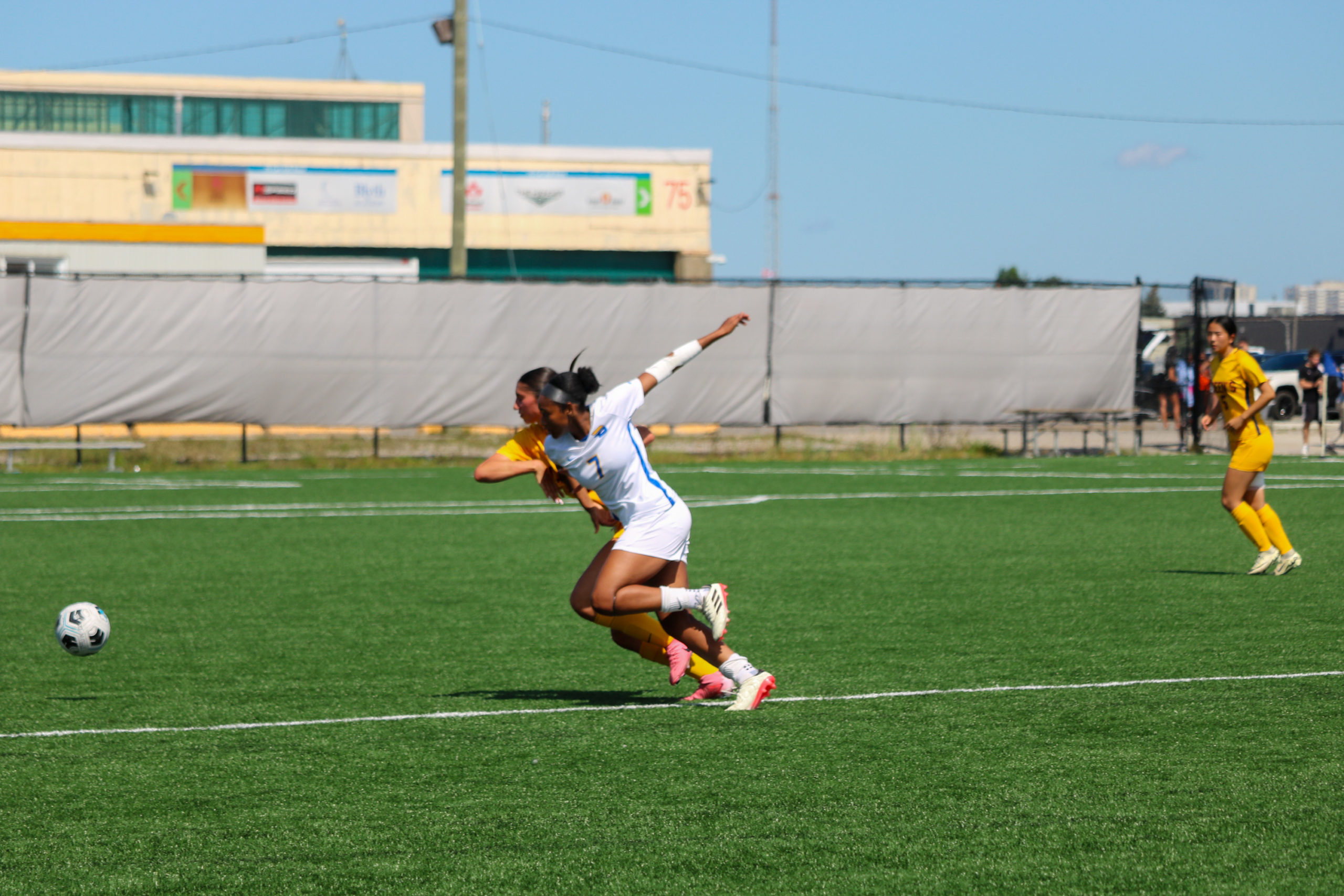 A TMU women's soccer player and a Queen's player chase a ball in lockstep.