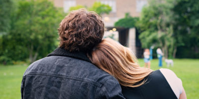 Two students sit in a field, with one leaning their head on the others shoulder