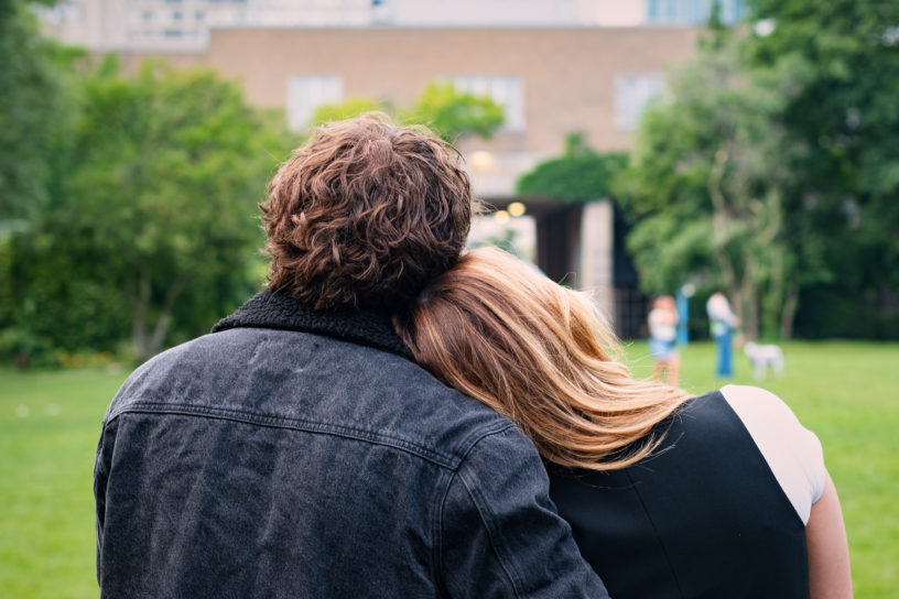 Two students sit in a field, with one leaning their head on the others shoulder