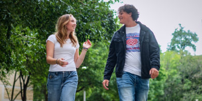 Two students converse while walking down a university campus