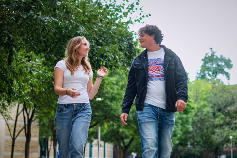 Two students converse while walking down a university campus