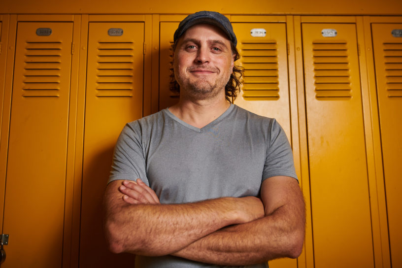 A middle-aged man smiles into the camera with his arms crossed.