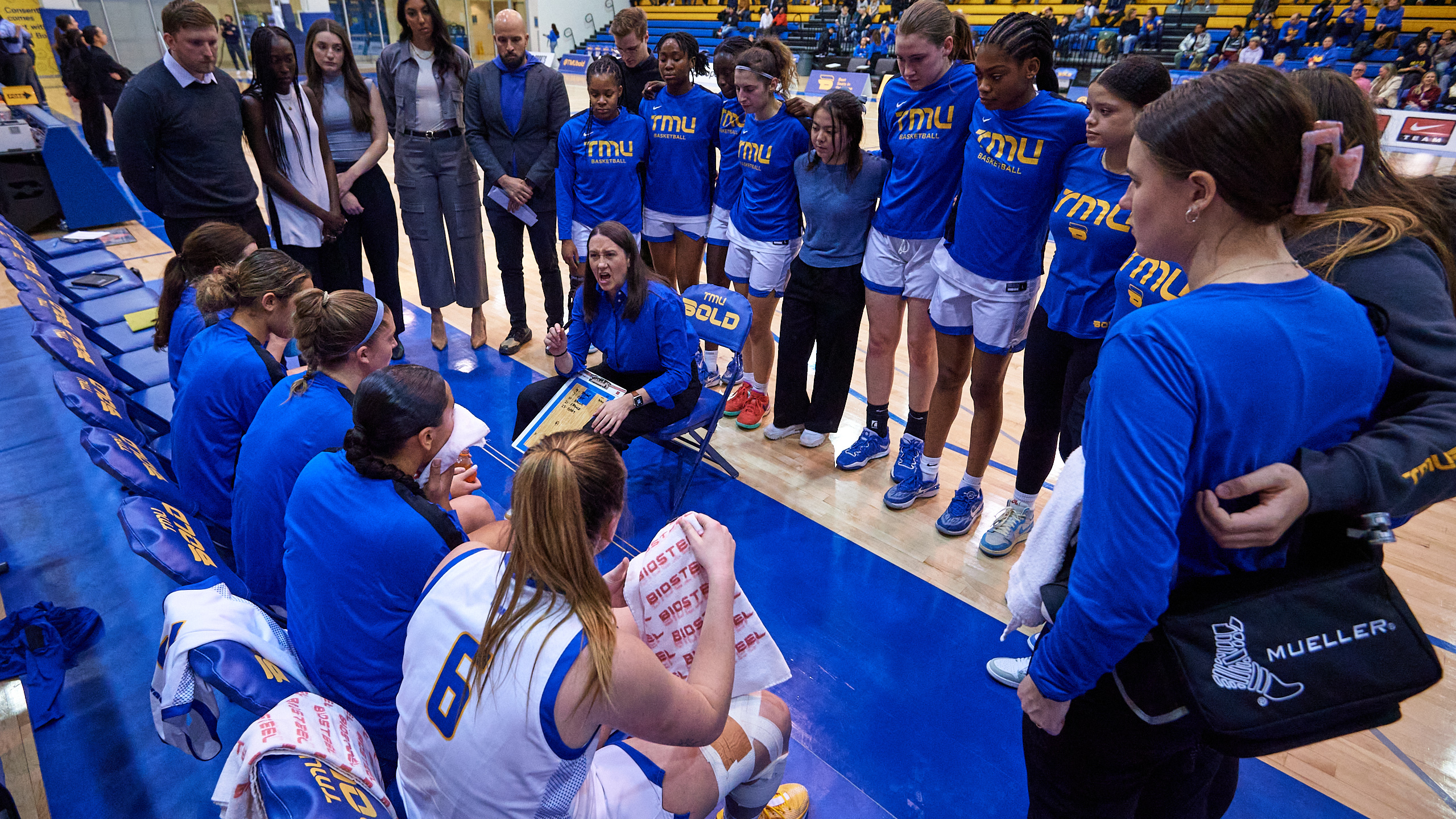 A female volleyball team huddles around their couch on the bench side