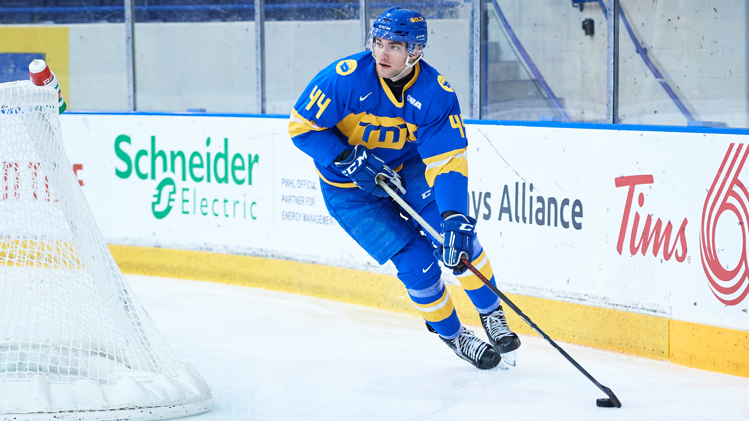 A hockey player in a blue uniform skates along the edge of the rink