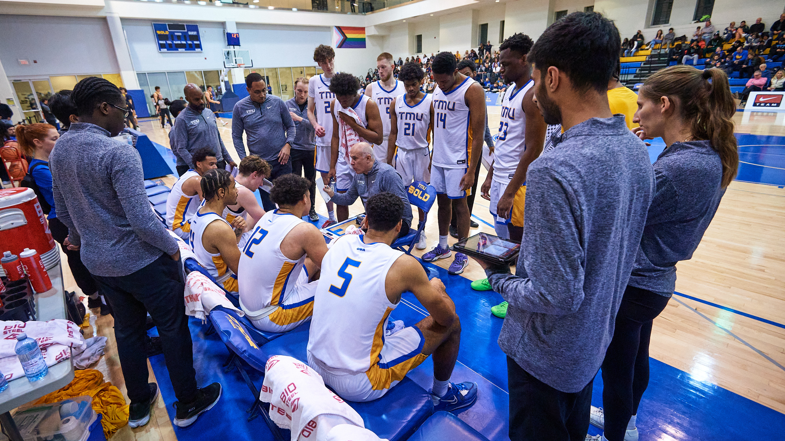 A male basketball team huddles around their coach on the bench