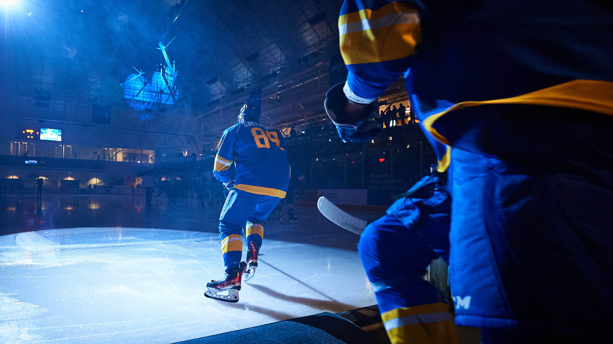 Two hockey players skate along an empty ice rink