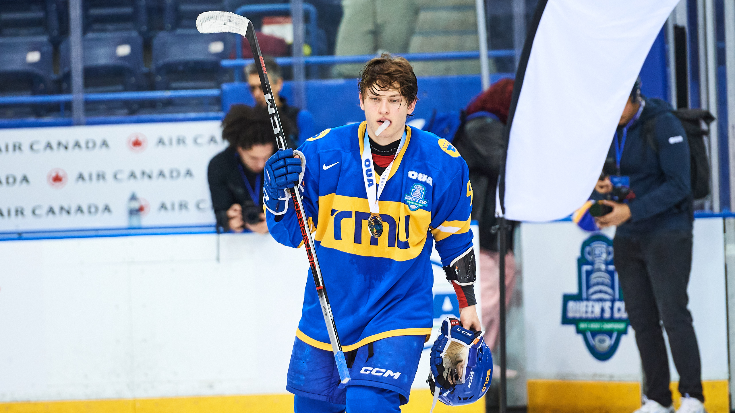 A hockey player enters the ice rink with their helmet in hand