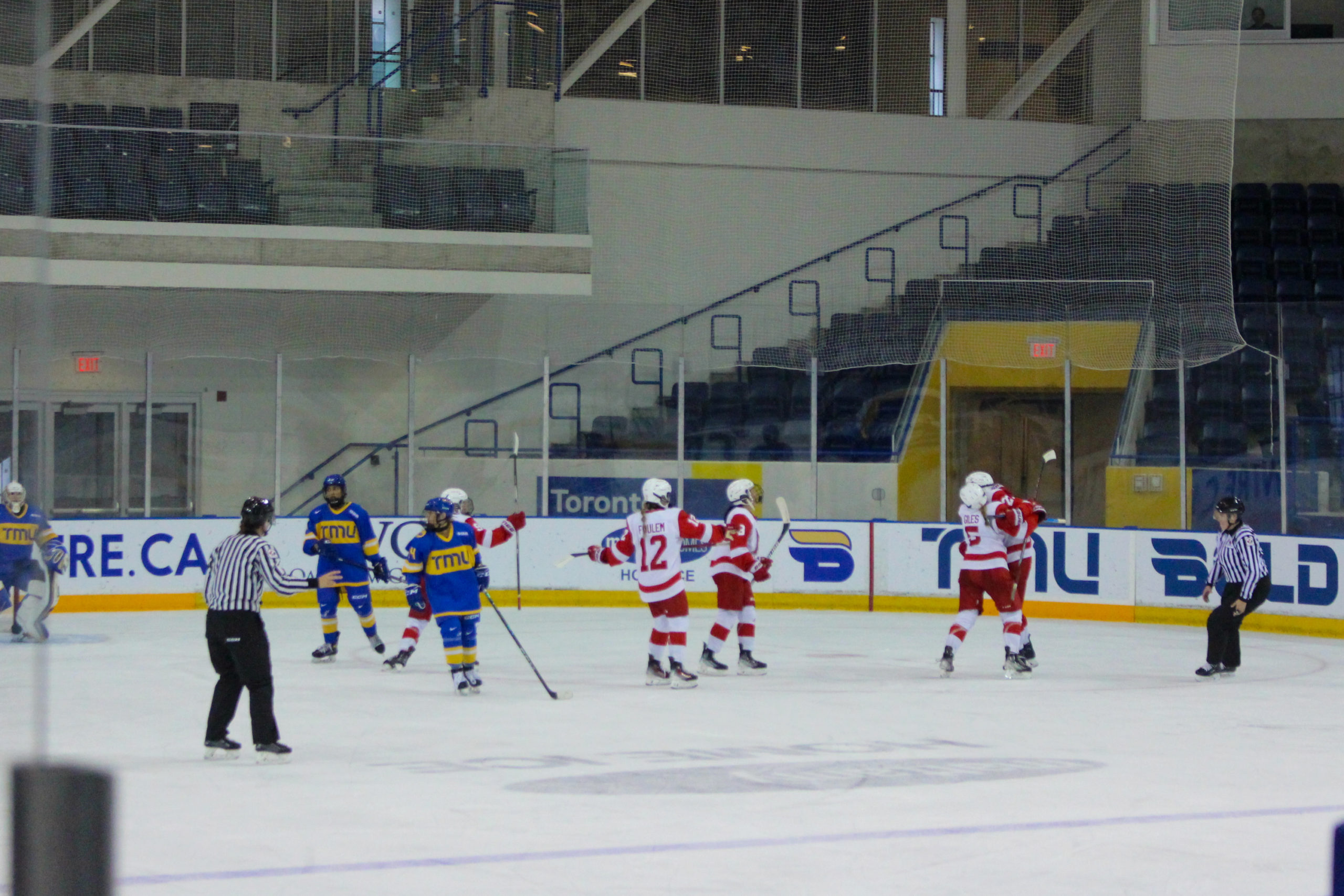 McGill Martlets hockey players gather to celebrate a goal while TMU players look at the bench or referees