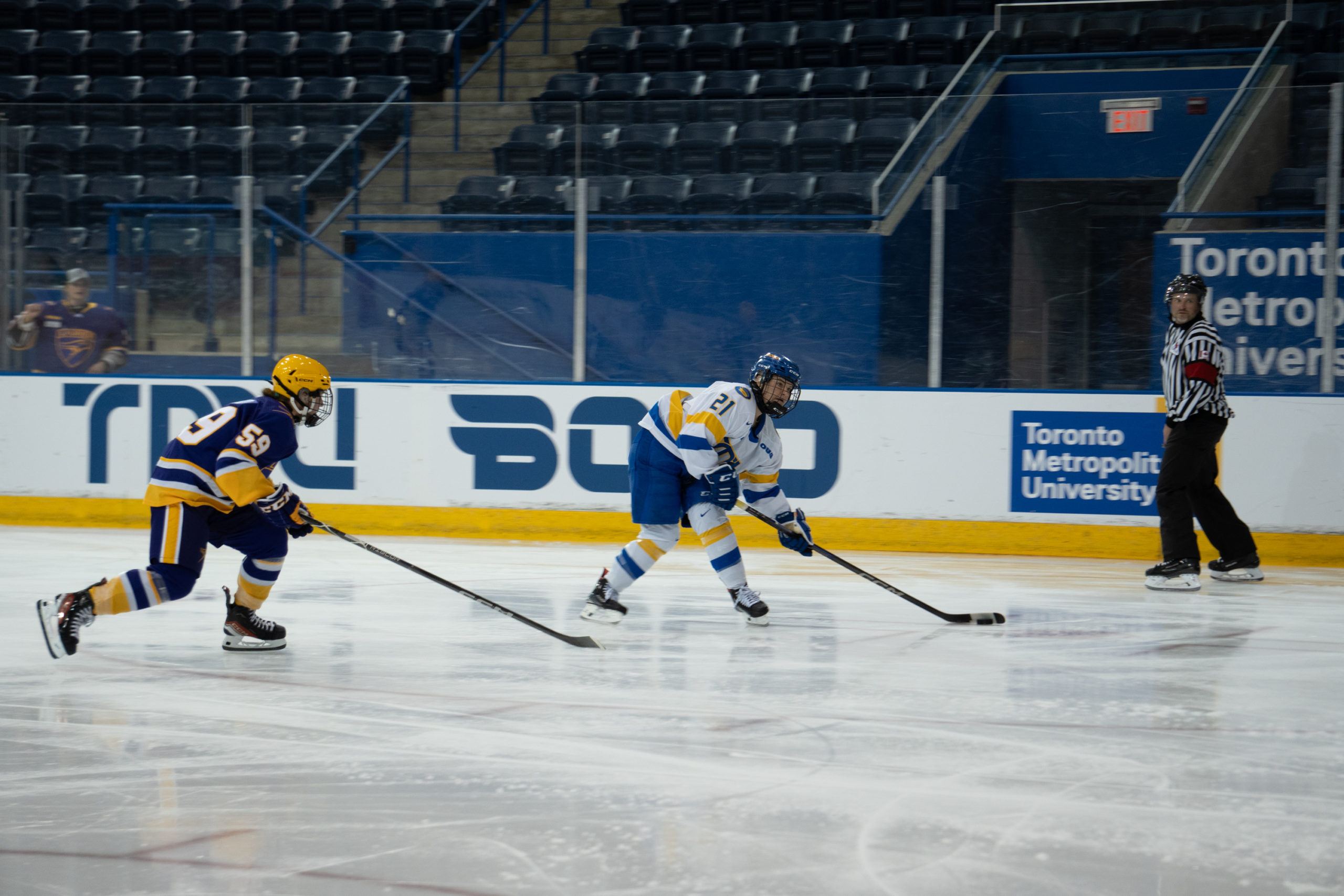 TMU Bold women's hockey player Emily Baxter prepares to shoot a puck as a Laurier Golden Hawks player reaches towards her with her stick.