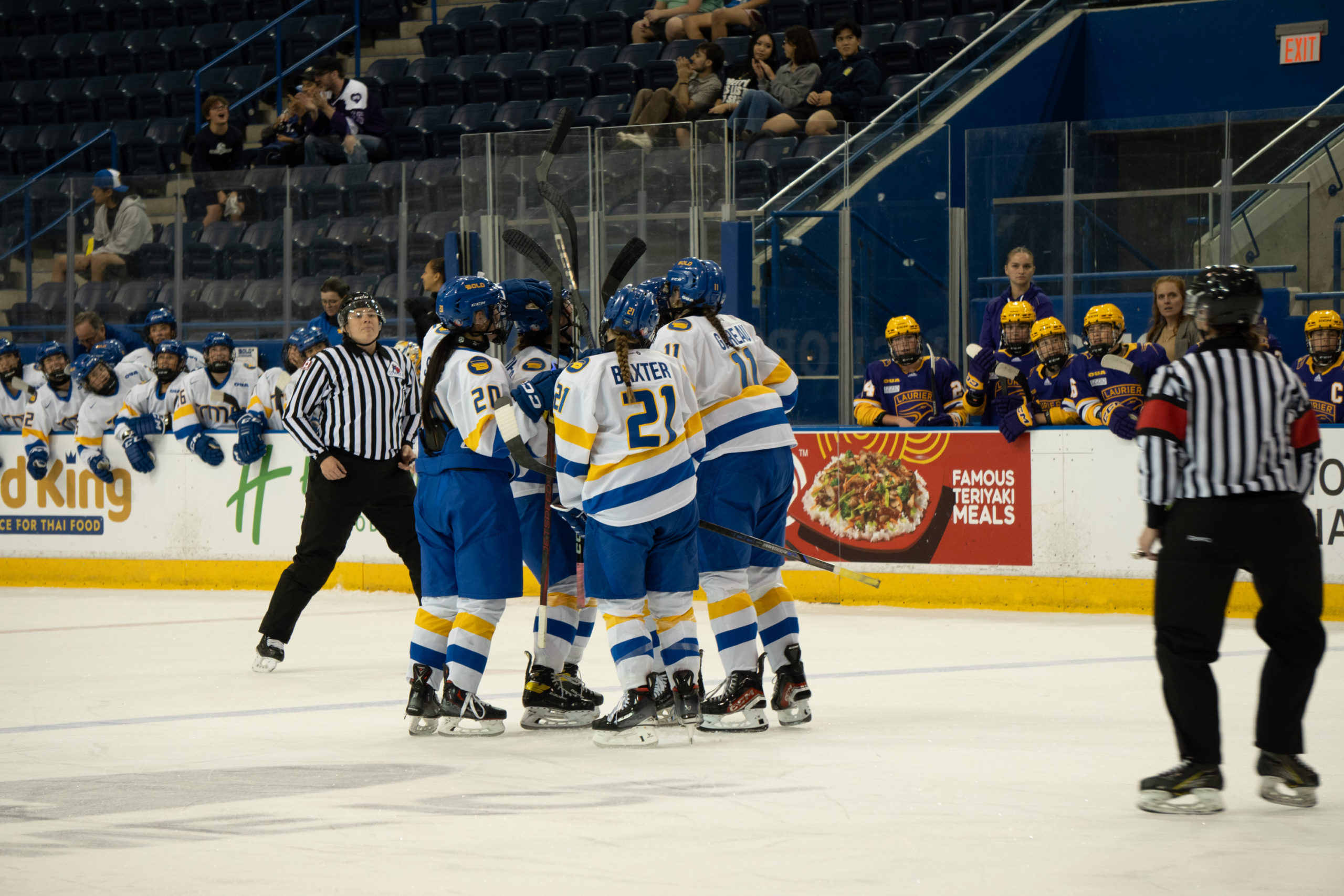 Members of the TMU Bold women's hockey team celebrate a goal. They are wearing white jerseys.