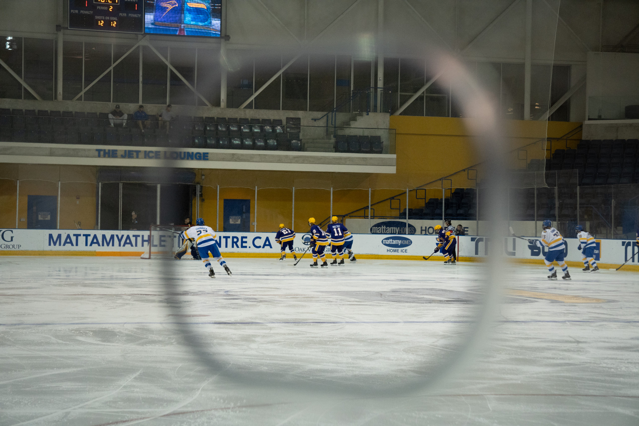 A photo through a photo hole at the MAC shows TMU and Laurier players playing hockey