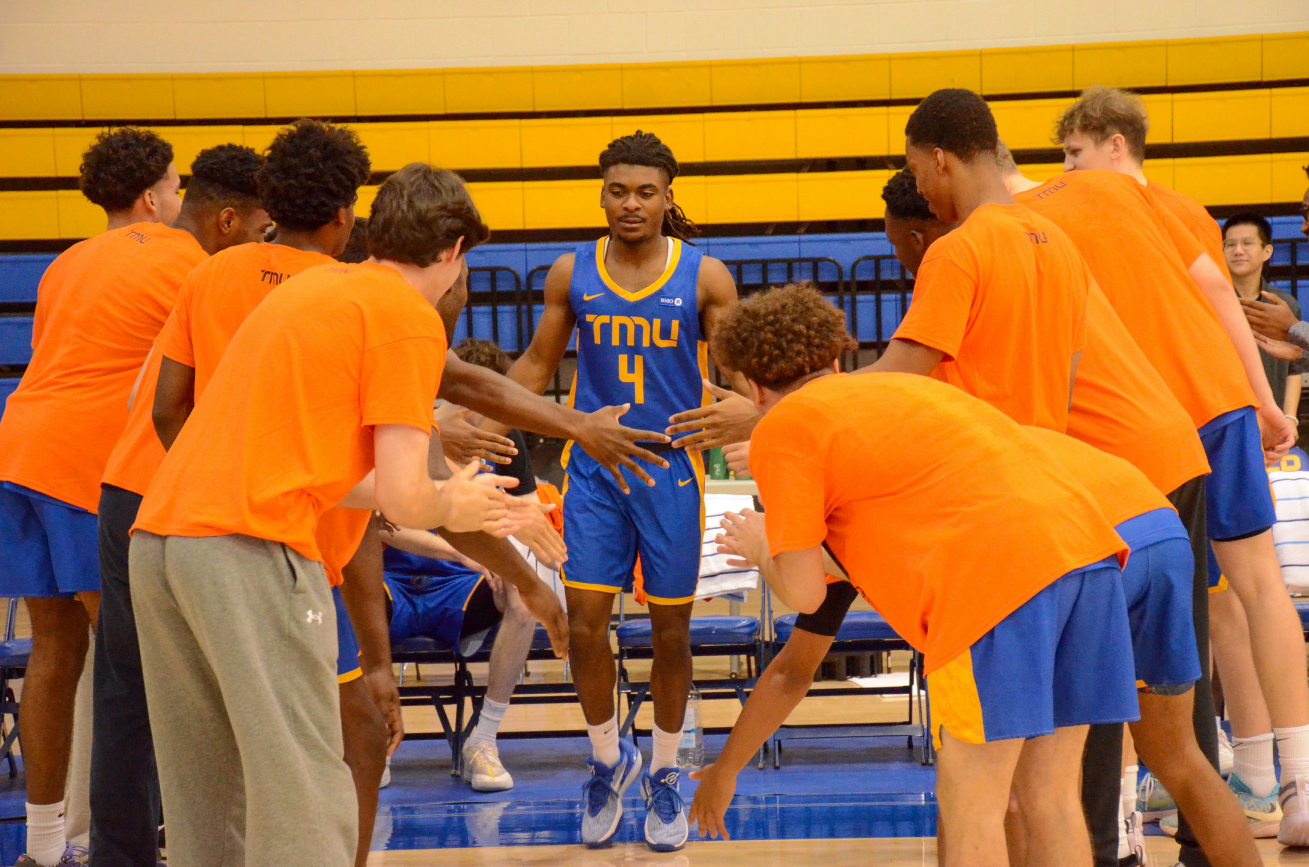 Maxine Louis-Jean high fives his teammates during line-up announcements. The bench players are wearing orange shirts.