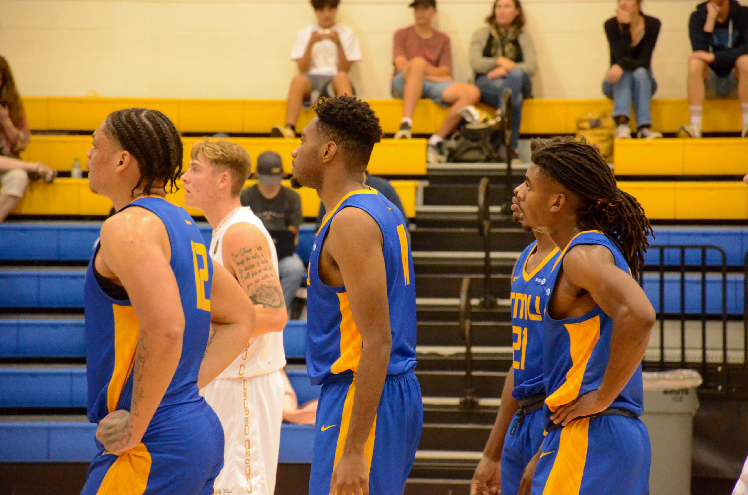 TMU Bold men's basketball players stand in a line as they watch a free throw