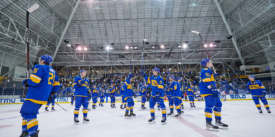 The TMU Bold men's hockey team celebrating with their sticks up high