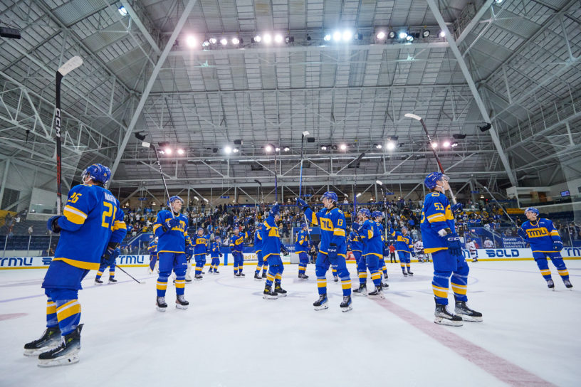 The TMU Bold men's hockey team celebrating with their sticks up high