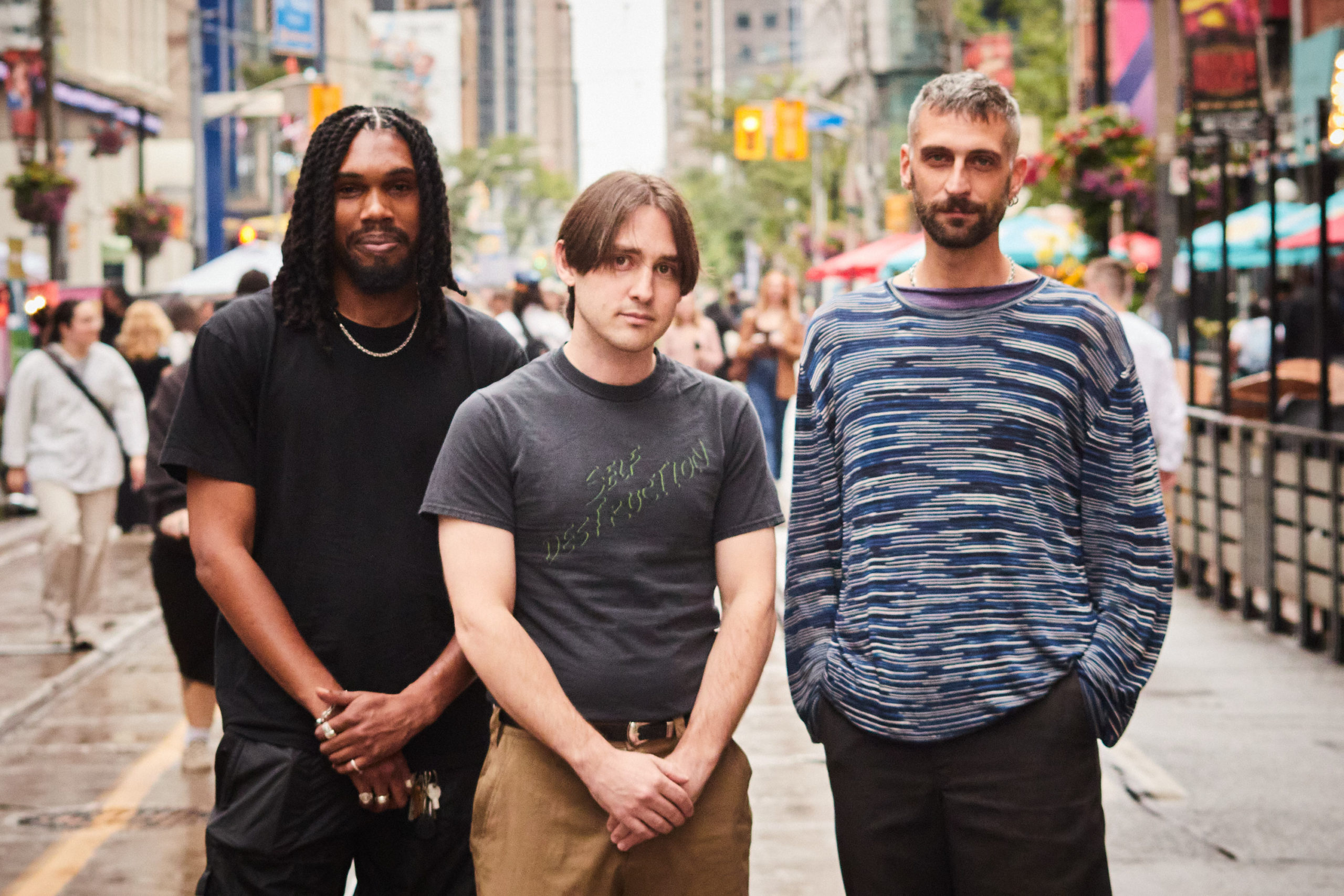 Three people stand in a busy street, looking towards the camera.