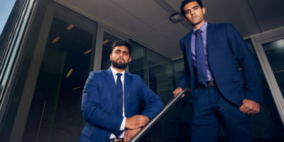 Two people in blue suits pose seriously standing on a stairway.