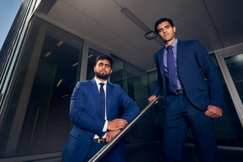 Two people in blue suits pose seriously standing on a stairway.