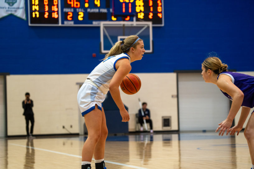 TMU Bold women's basketball player Kaillie Hall dribbles a basketball as a Bishop's Gaiters player approaches her