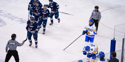 U of T Varsity Blues men's hockey players skate to their bench in a line after scoring, while TMU players stand around