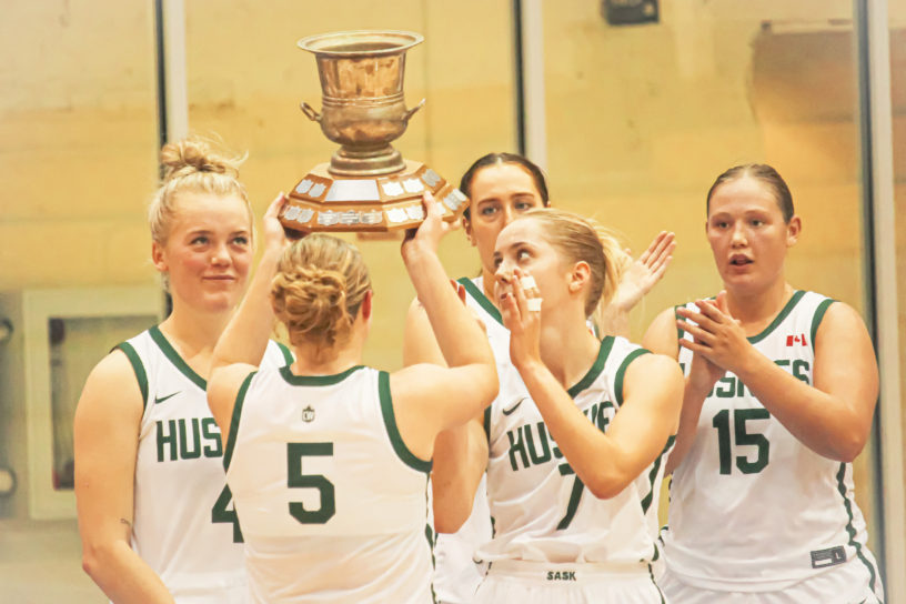 Saskatchewan Huskies guard Gage Grassick lifts the Darcel Wright Memorial Classic trophy over her head with her teammates