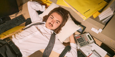 An office worker lays down with a pillow over their desk.