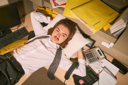 An office worker lays down with a pillow over their desk.