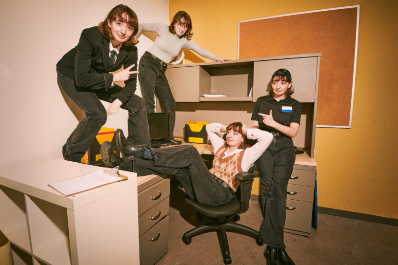 A composite image of 4 versions of Sarah standing around the desk making various funny poses.