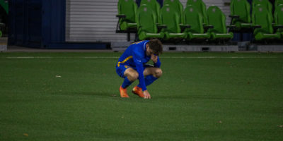 Benjamin Dunn crouching to the ground on a soccer pitch with his head in his hands