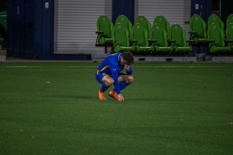 Benjamin Dunn crouching to the ground on a soccer pitch with his head in his hands