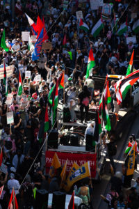 A protestor speaks into a microphone on top of a stage surrounded by a crowd.