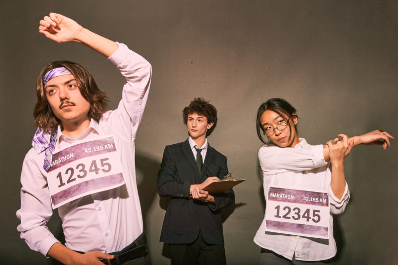 A photo composite of two prospective empoyees wearing marathon bibs, with an employer in the centre holding a clipboard.