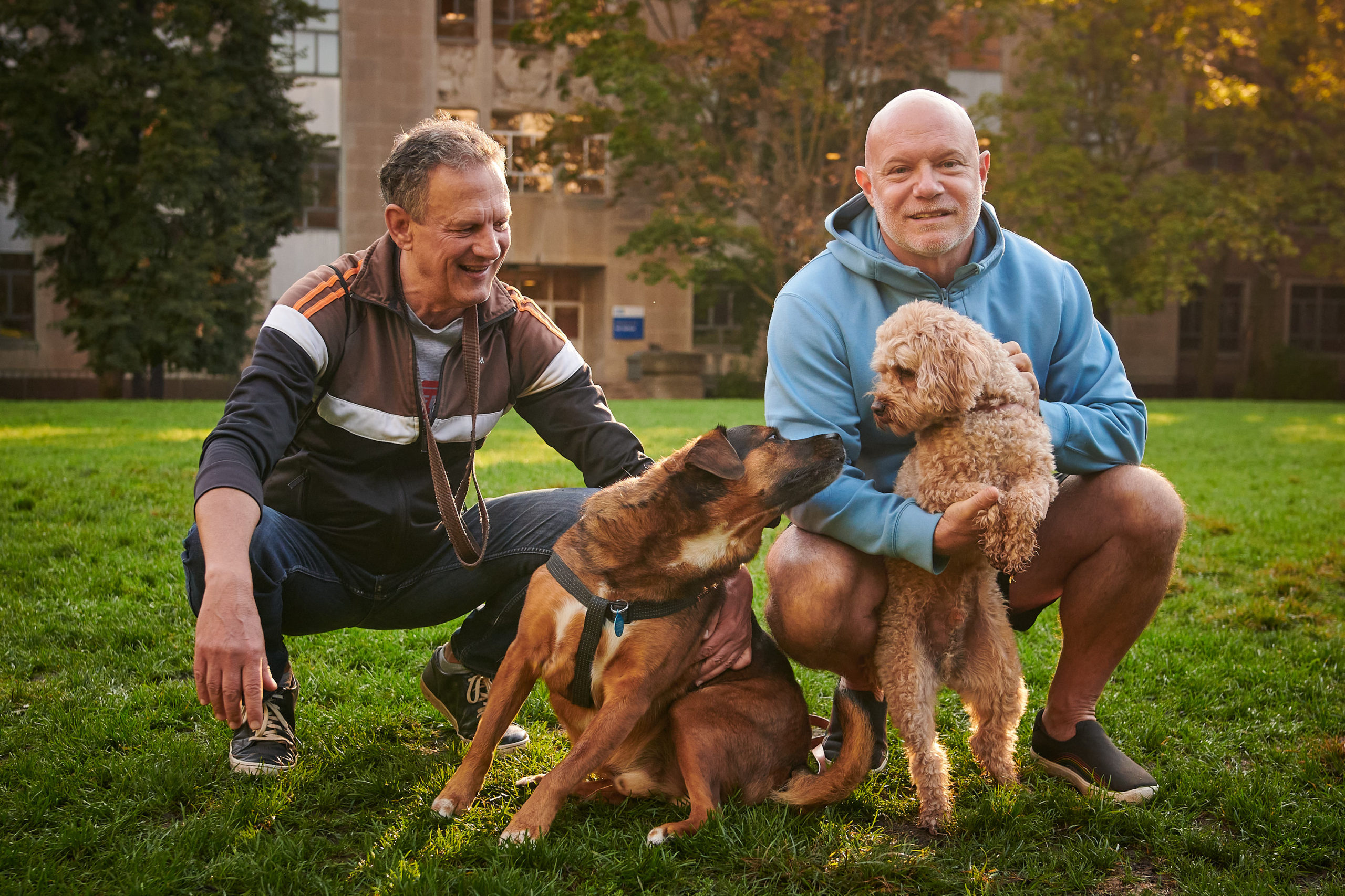 Two dogs small each other, with their owners standing beside them bent down.