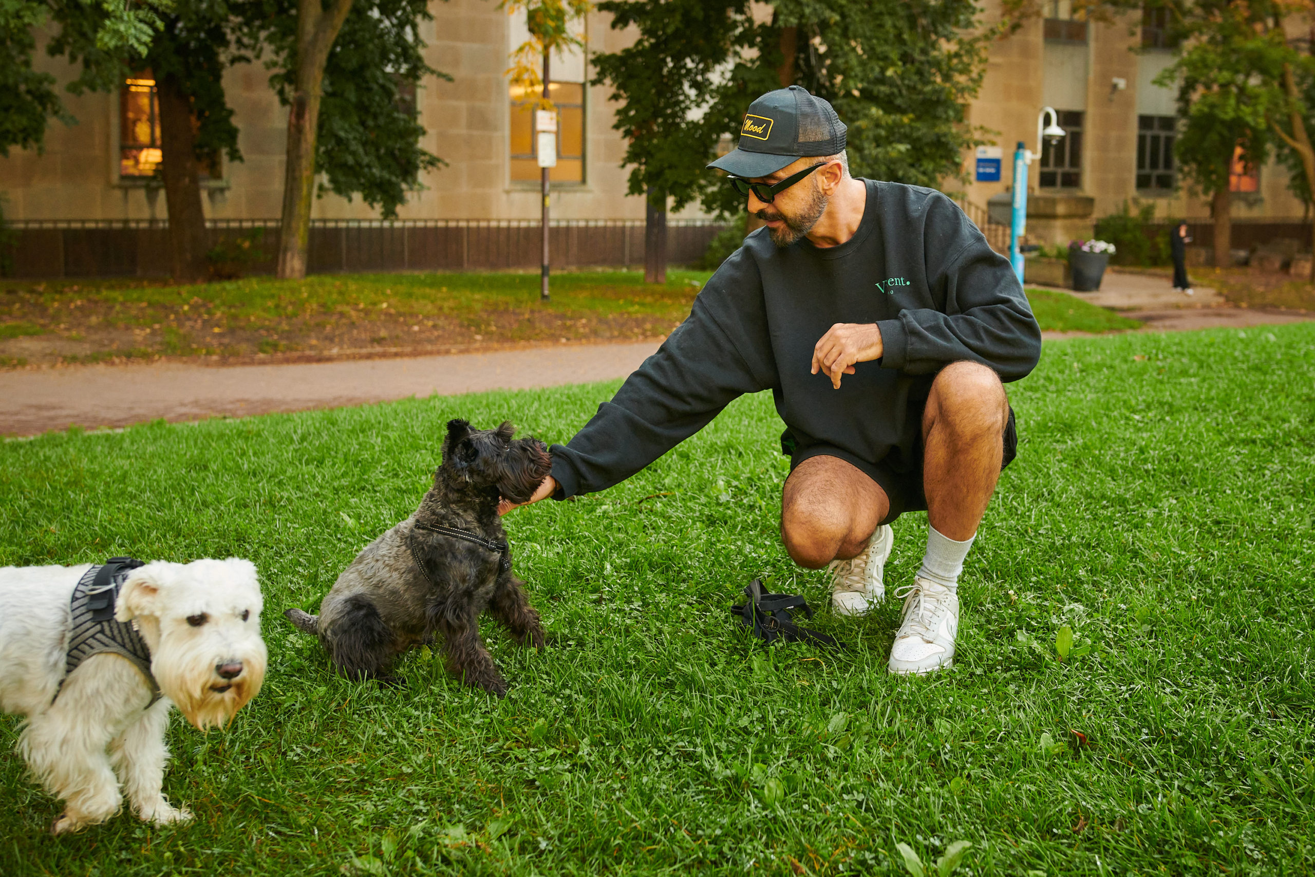 A dog owner pets their dog in a park field.