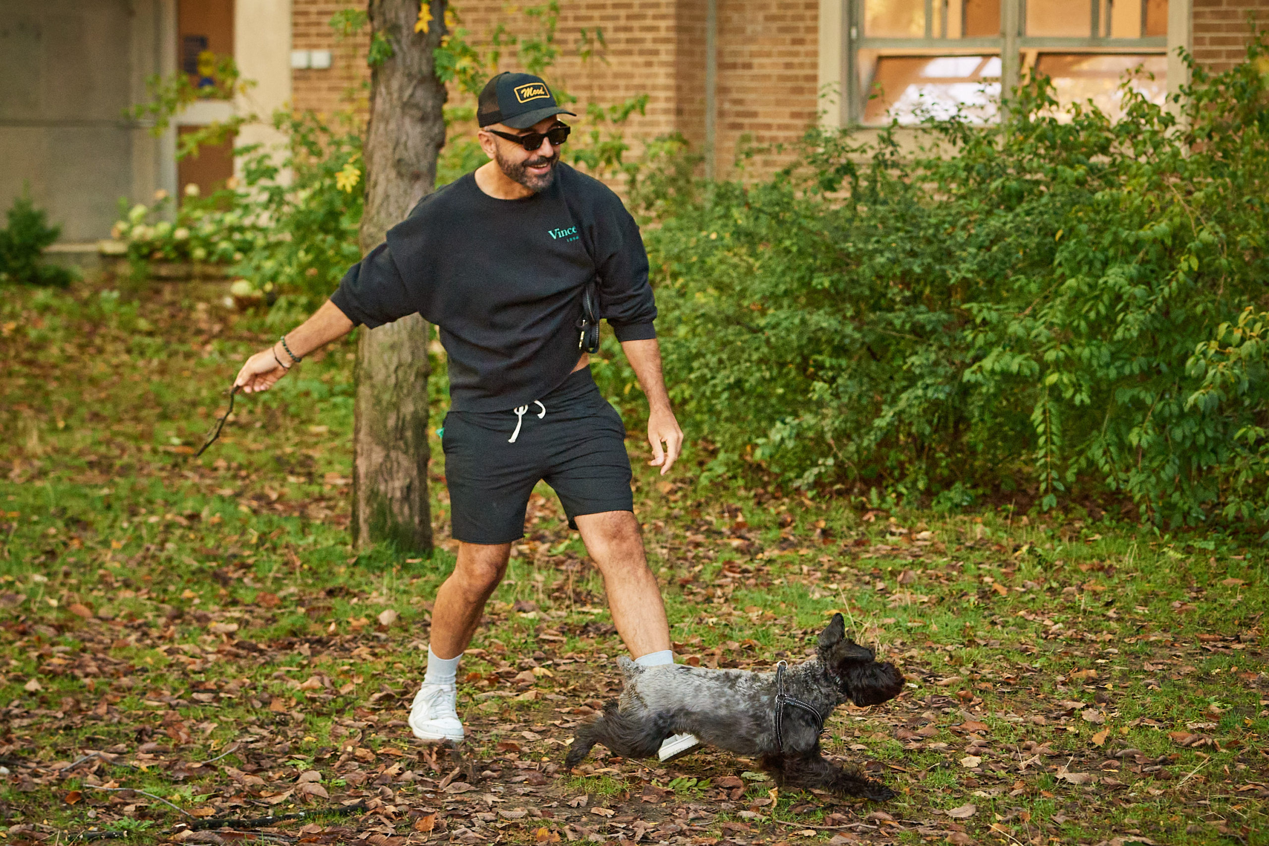 A dog owner plays catch with their dog in a park field in front of a university building.