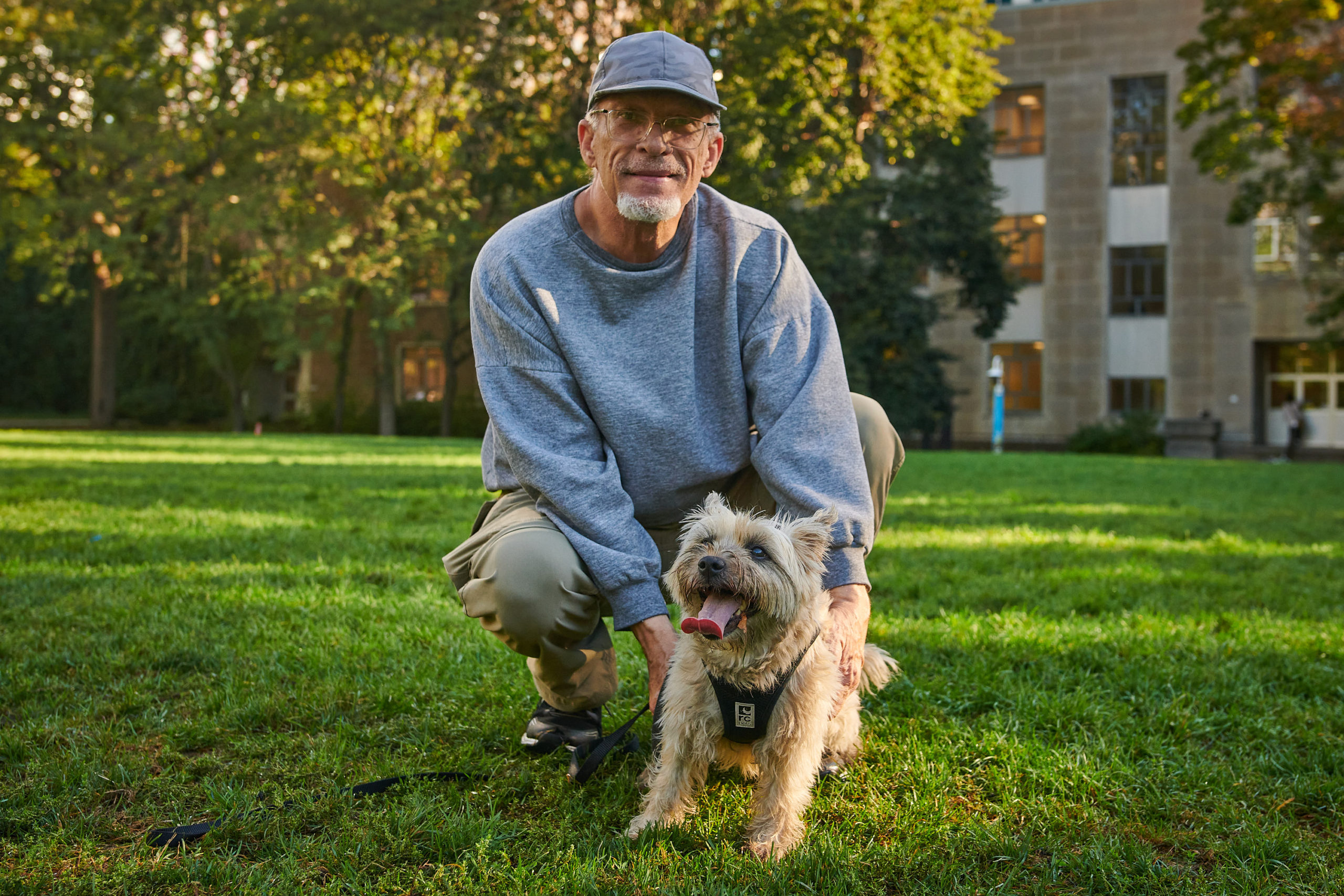 A dog owner bends down to stand beside their excited pet in a park field.