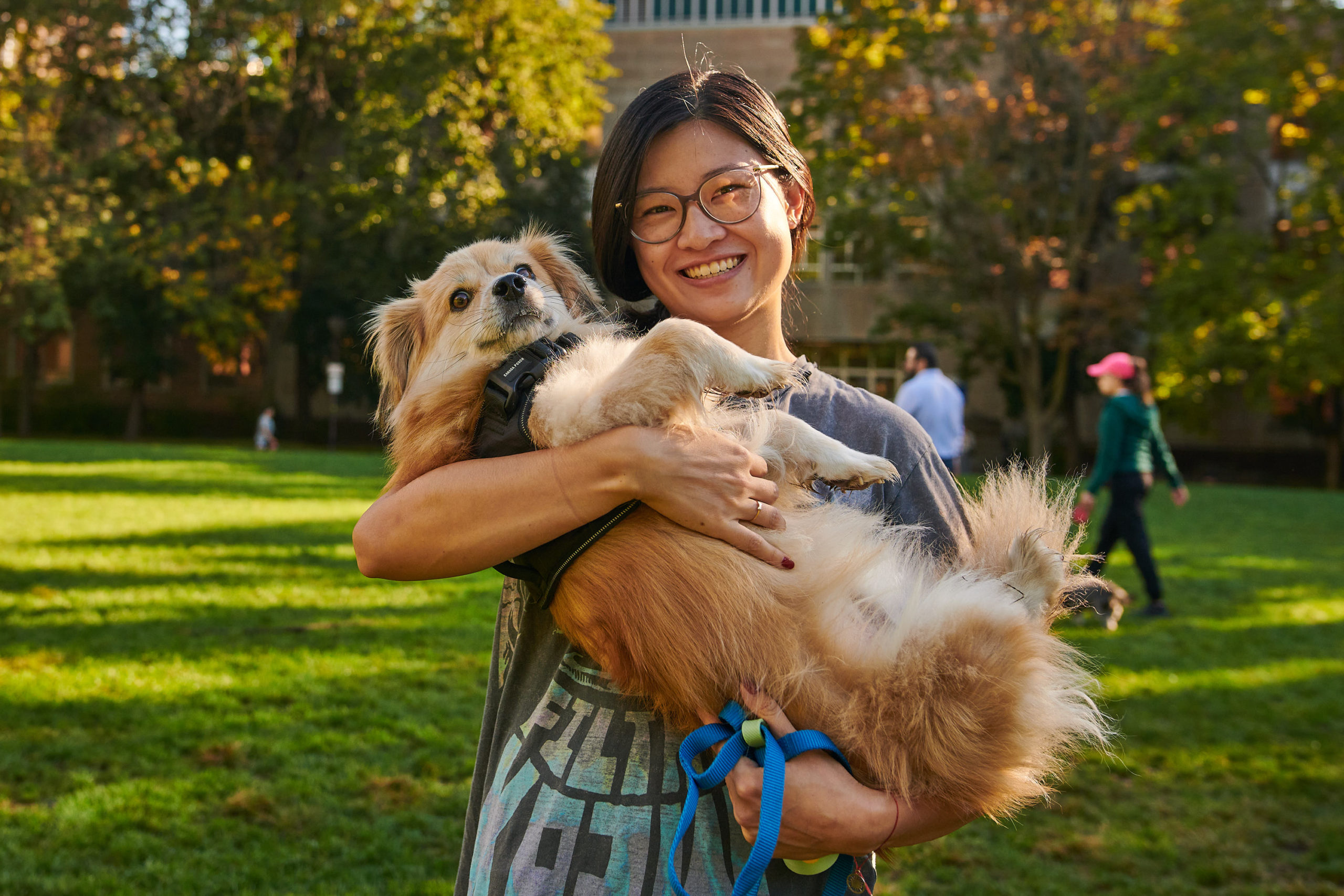 A dog owner holds their dog in their arms and smiles in a green field.