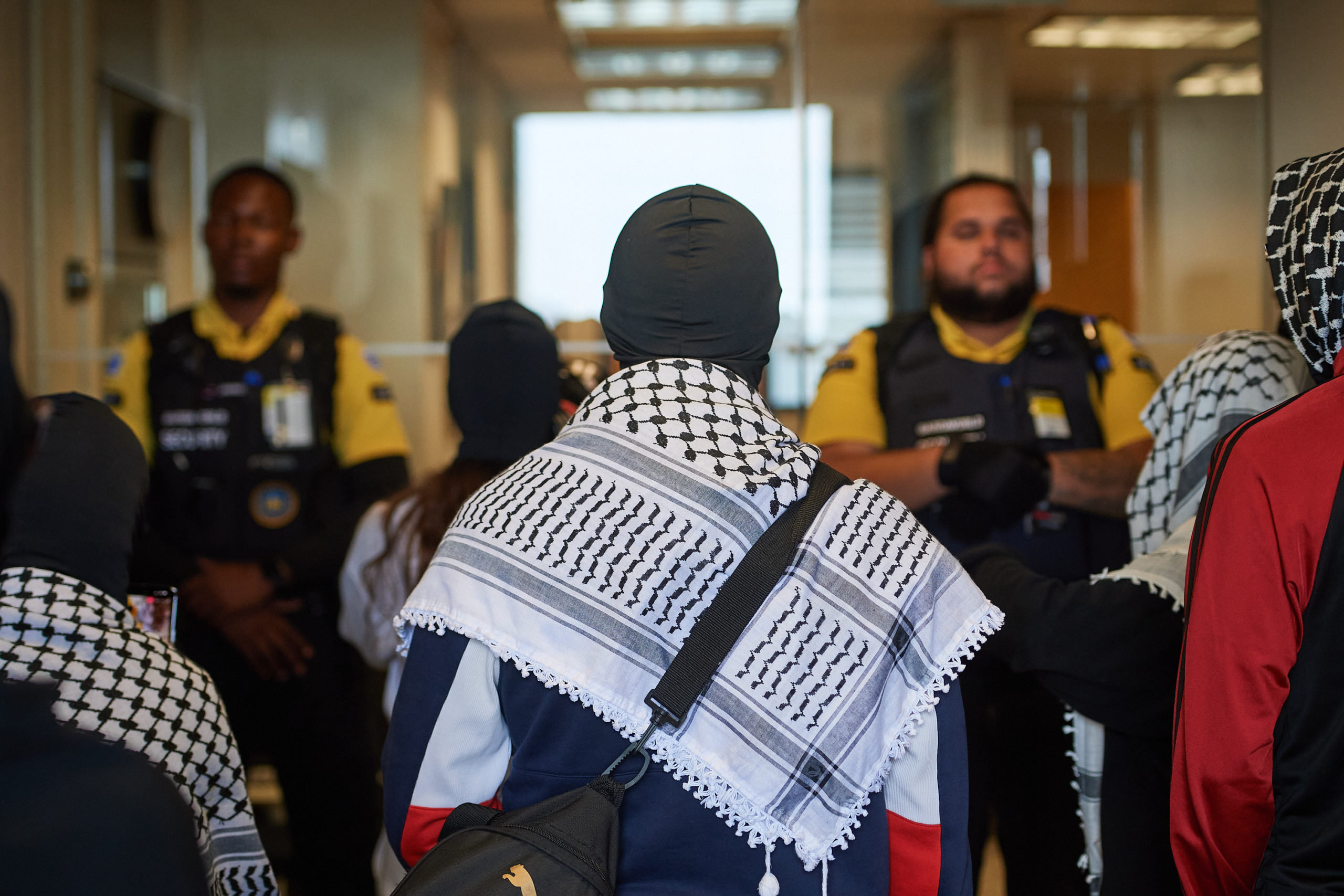 demonstrators articulate demands through megaphone at glass door flanked by two security guards