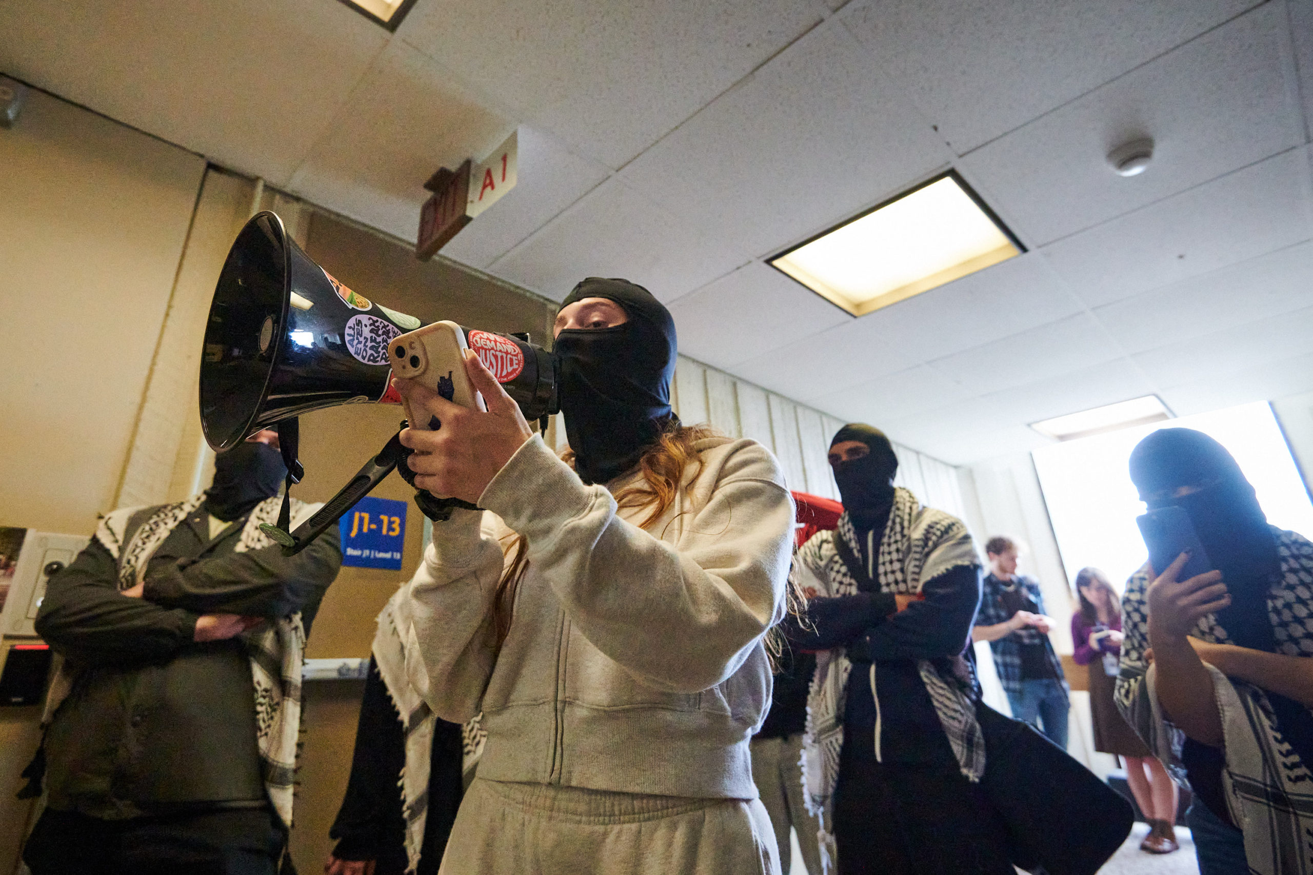 demonstrators articulate demands through megaphone at glass door