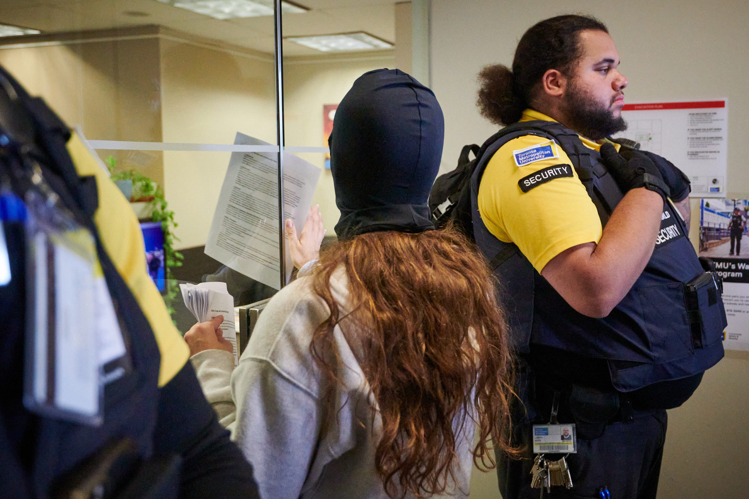 demonstrators articulate demands through megaphone and put letters through door flanked by two security guards