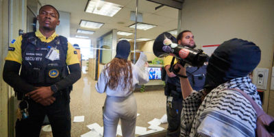 demonstrators articulate demands through megaphone and put letters through door flanked by two security guards