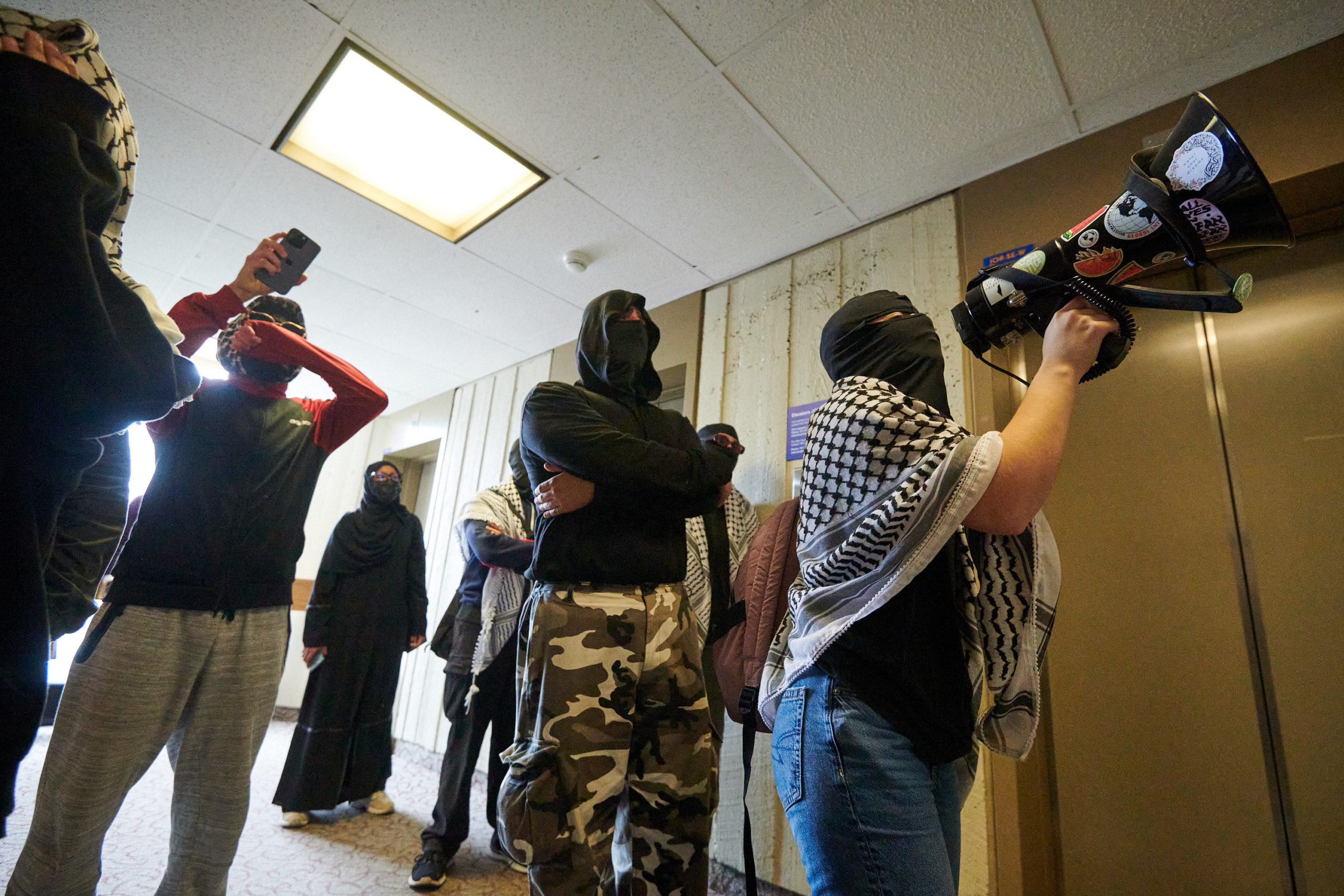 demonstrators articulate demands through megaphone at glass door flanked by two security guards