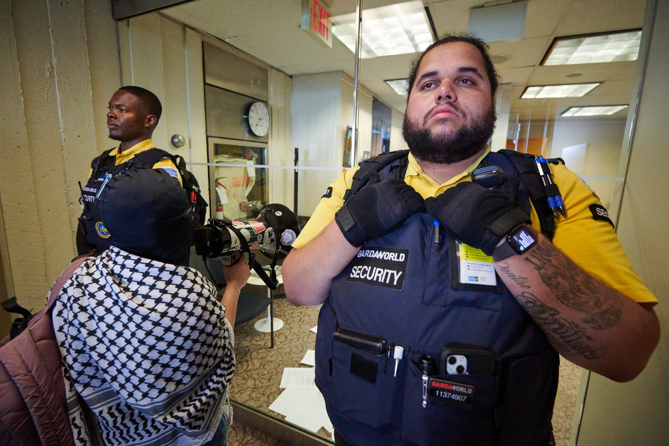 demonstrators articulate demands through megaphone and put letters through door flanked by two security guards